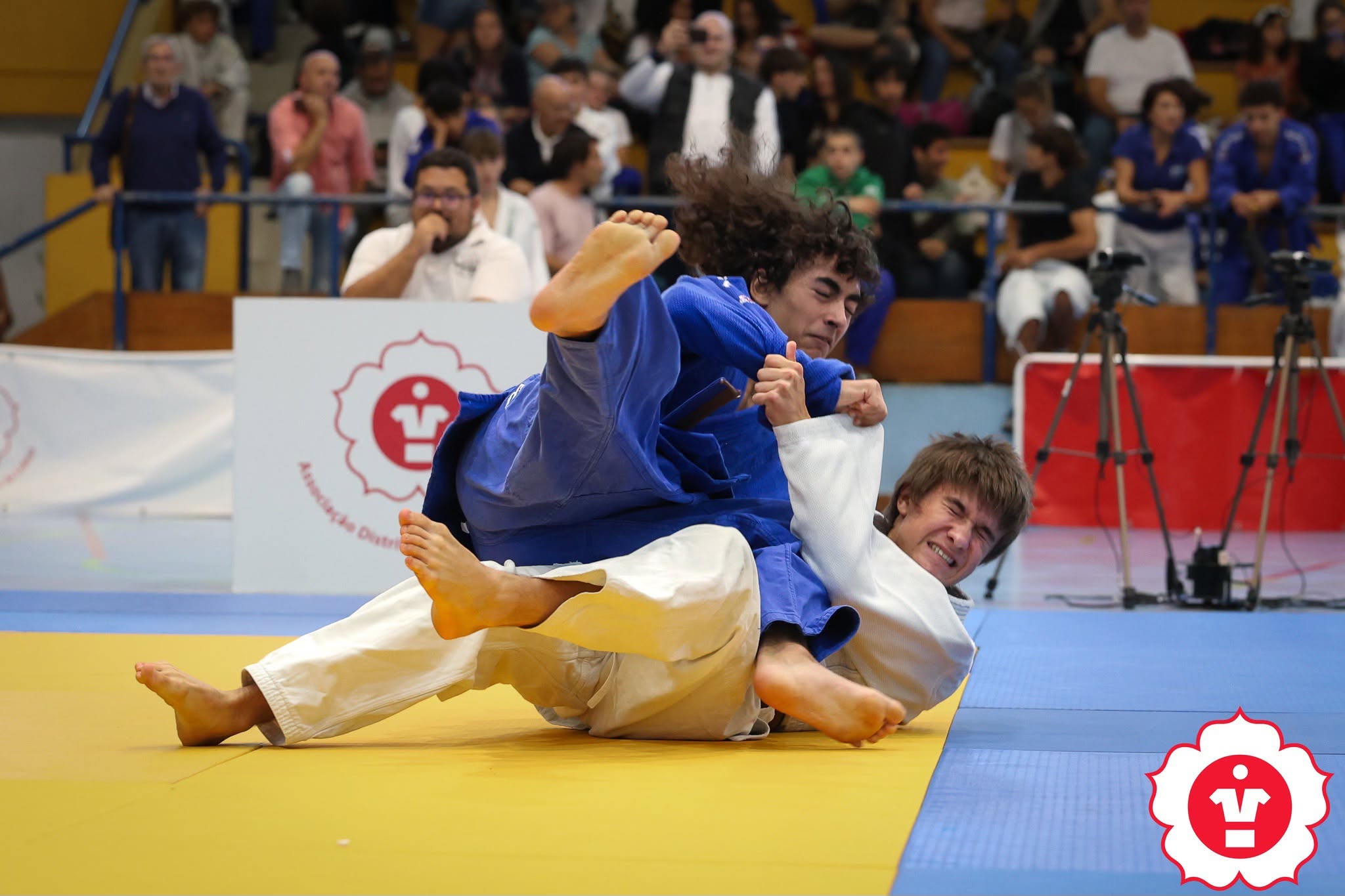 Dois judocas disputam um combate no tatami amarelo.